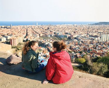 Two students are sitting on a hill and overlooking the city of Barcelona.